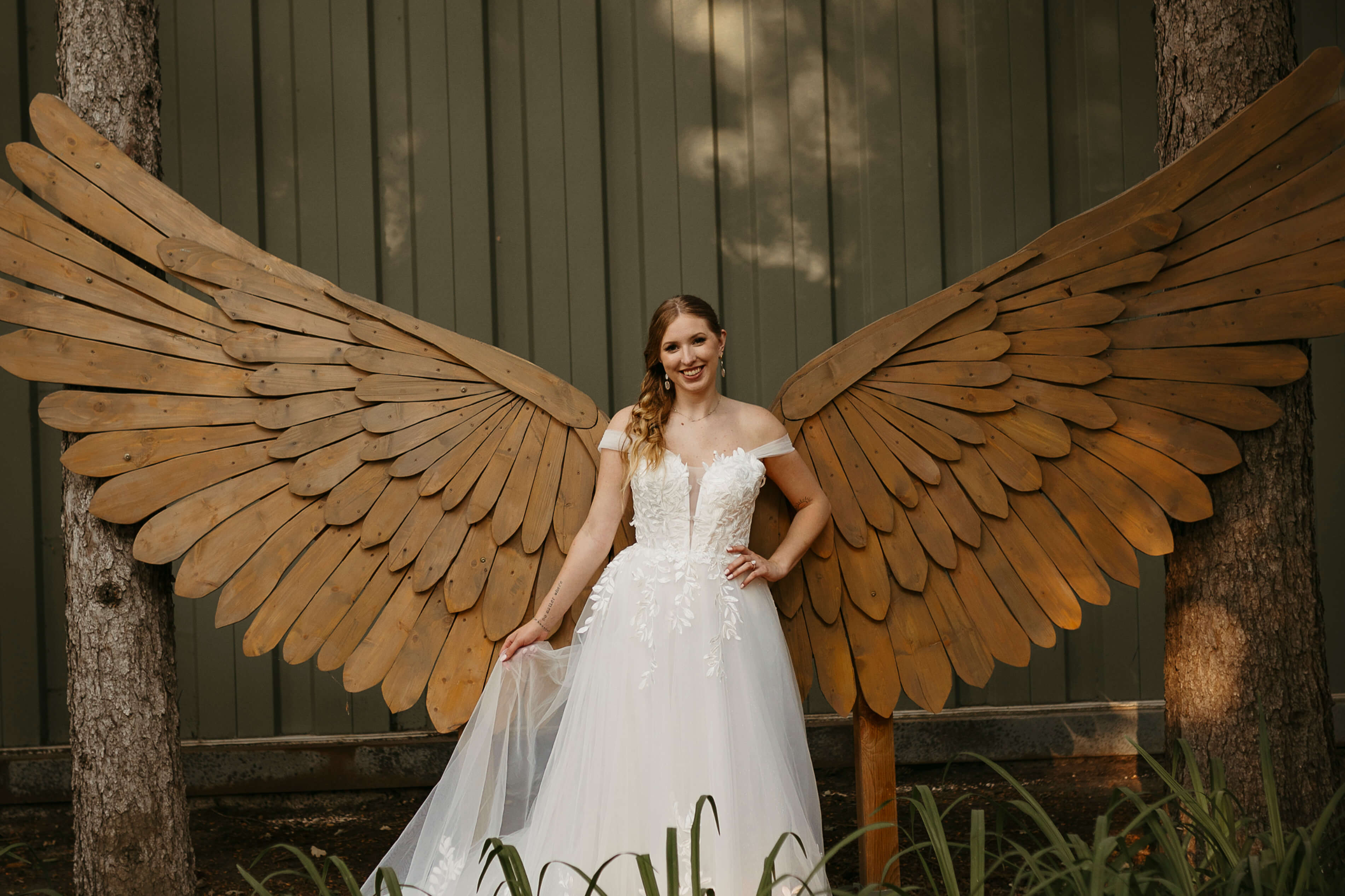 A bride wearing a white dress, and standing in-front of wooden designed wings.