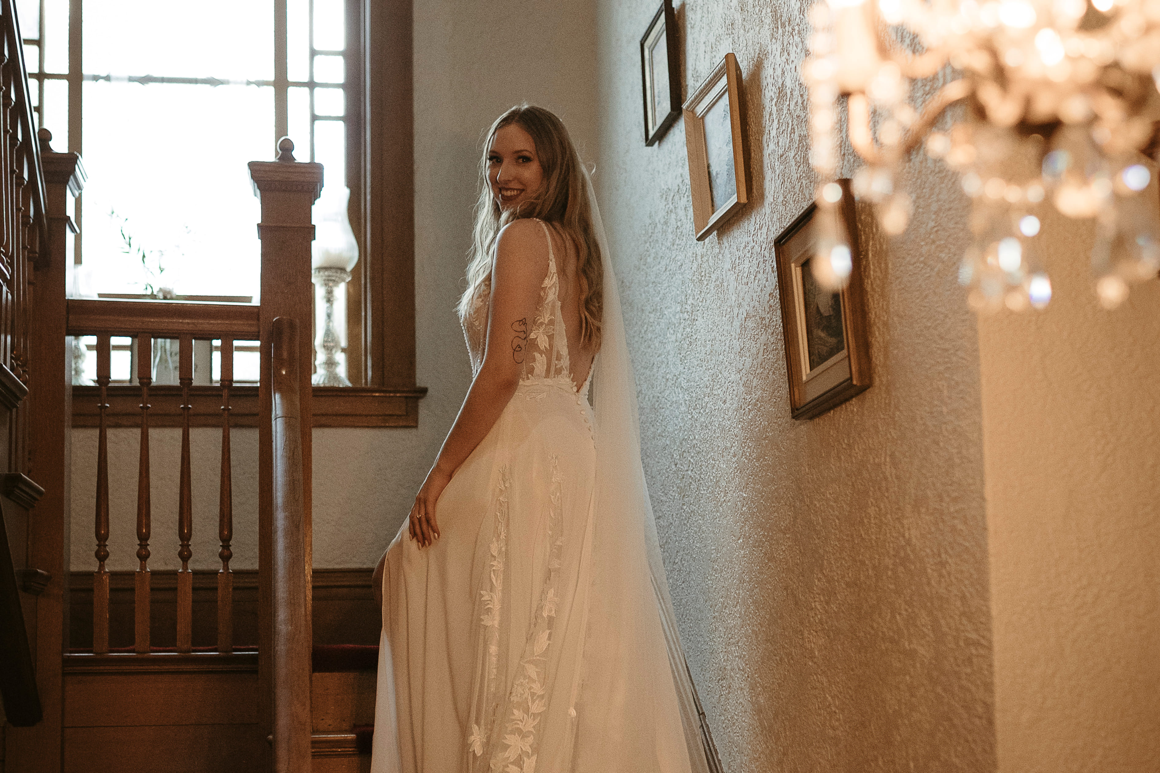 A bide wearing a white wedding dress while sitting on a white fancy chair and leaning over to put her high heel on.