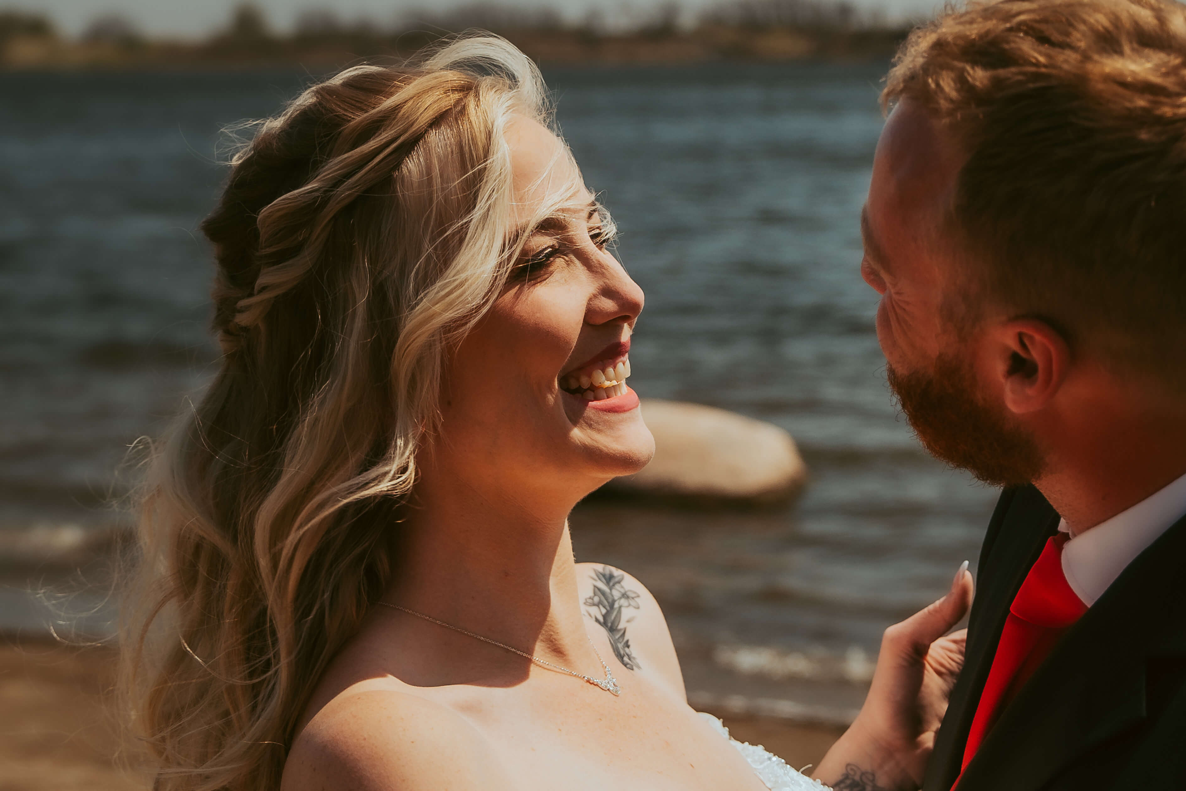 Bride with her husband laughing and smiling with the lake in the background.